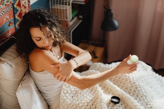 Woman applying skincare lotion in a cozy bedroom, focusing on relaxation and self-care.